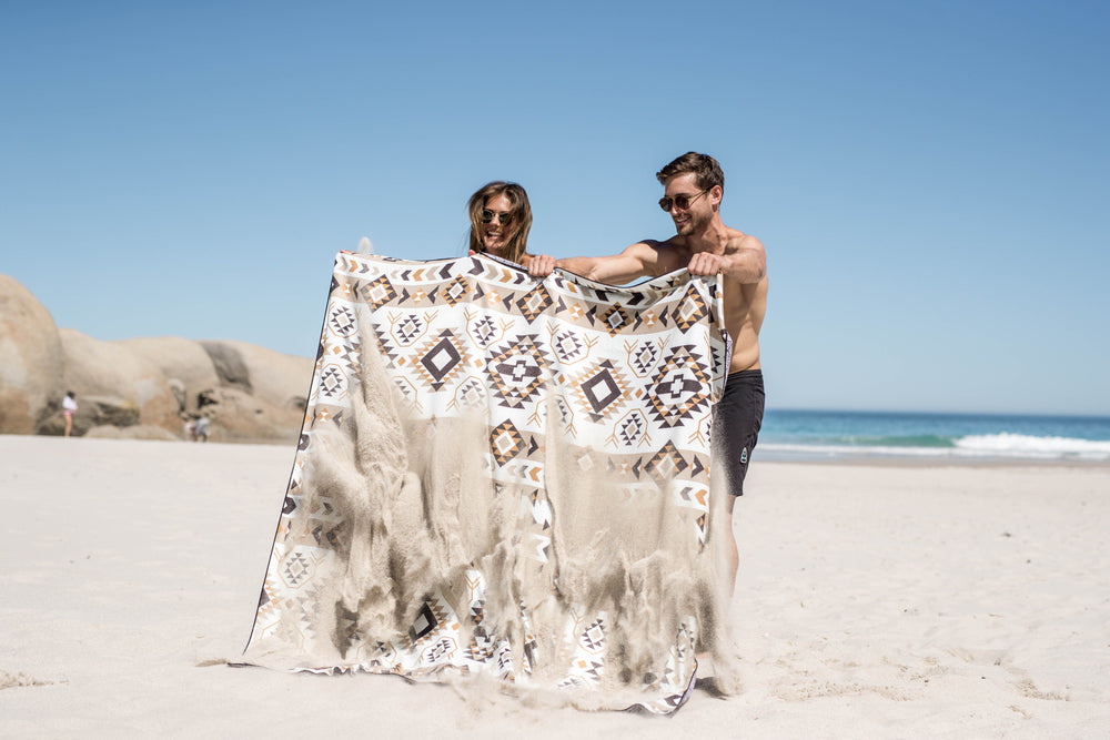 Couple holding up an Aztec-print Tesalate sand-free beach blanket