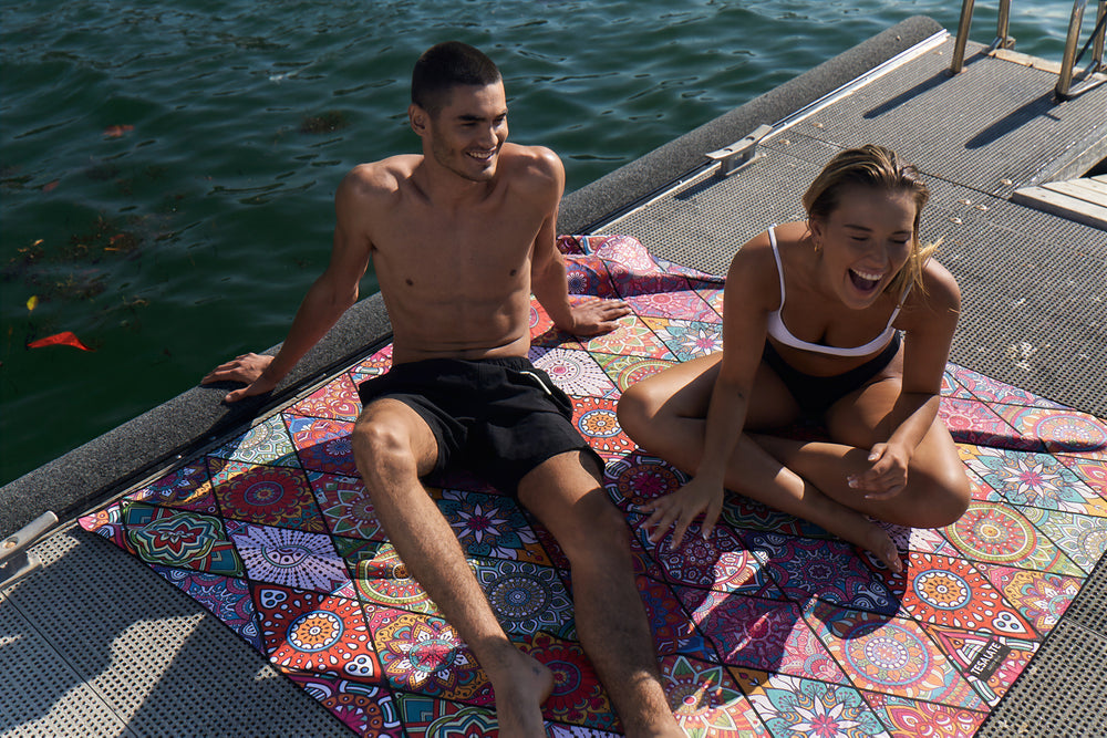 Couple relaxing on a mandala-print Tesalate beach blanket on a pontoon
