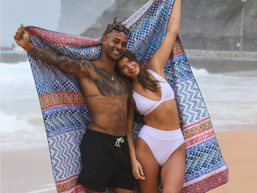 Couple wrapped in a blue patterned Tesalate beach blanket at the beach